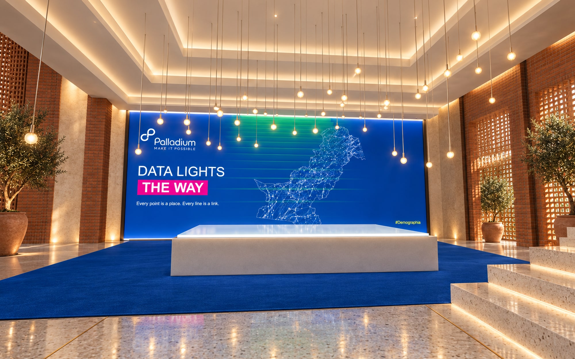 A wall-sized map of Pakistan drawn as glowing points and lines, a lit table in front of it and dozens of small lamps hanging above the table at different heights