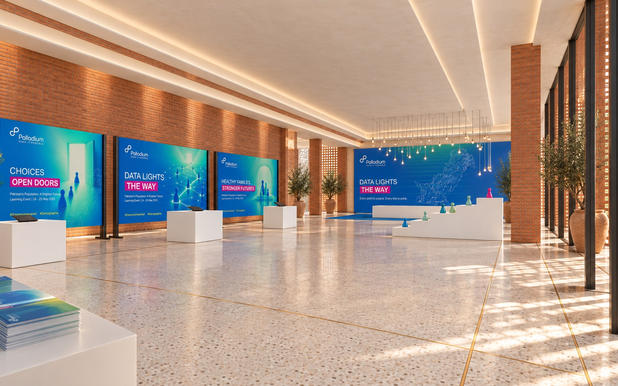 A long exhibition room with message panels on frames along one side, a plinth and a tablet before each, a table of booklets in the foreground and a map wall at the far end