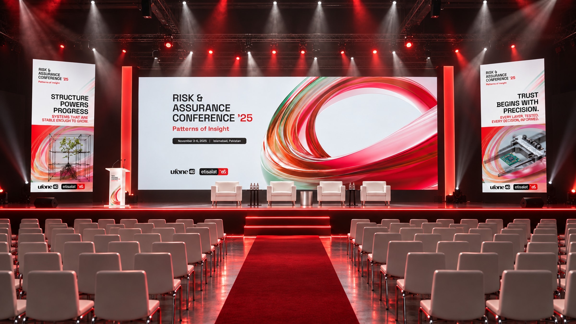 The plenary hall: a wide screen carrying the Risk & Assurance Conference '25 key visual, a glass ribbon in red, green and white, between two portrait screens, above a stage with a lectern and four white armchairs, rows of white chairs either side of a red aisle