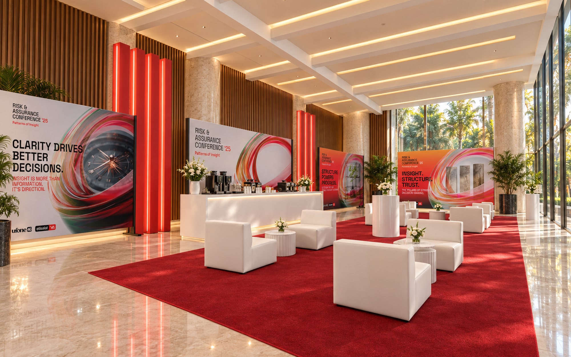 A networking lounge with white armchairs on a red rug, high tables, a white coffee bar between fins of red light, and branding panels on frames along the wall