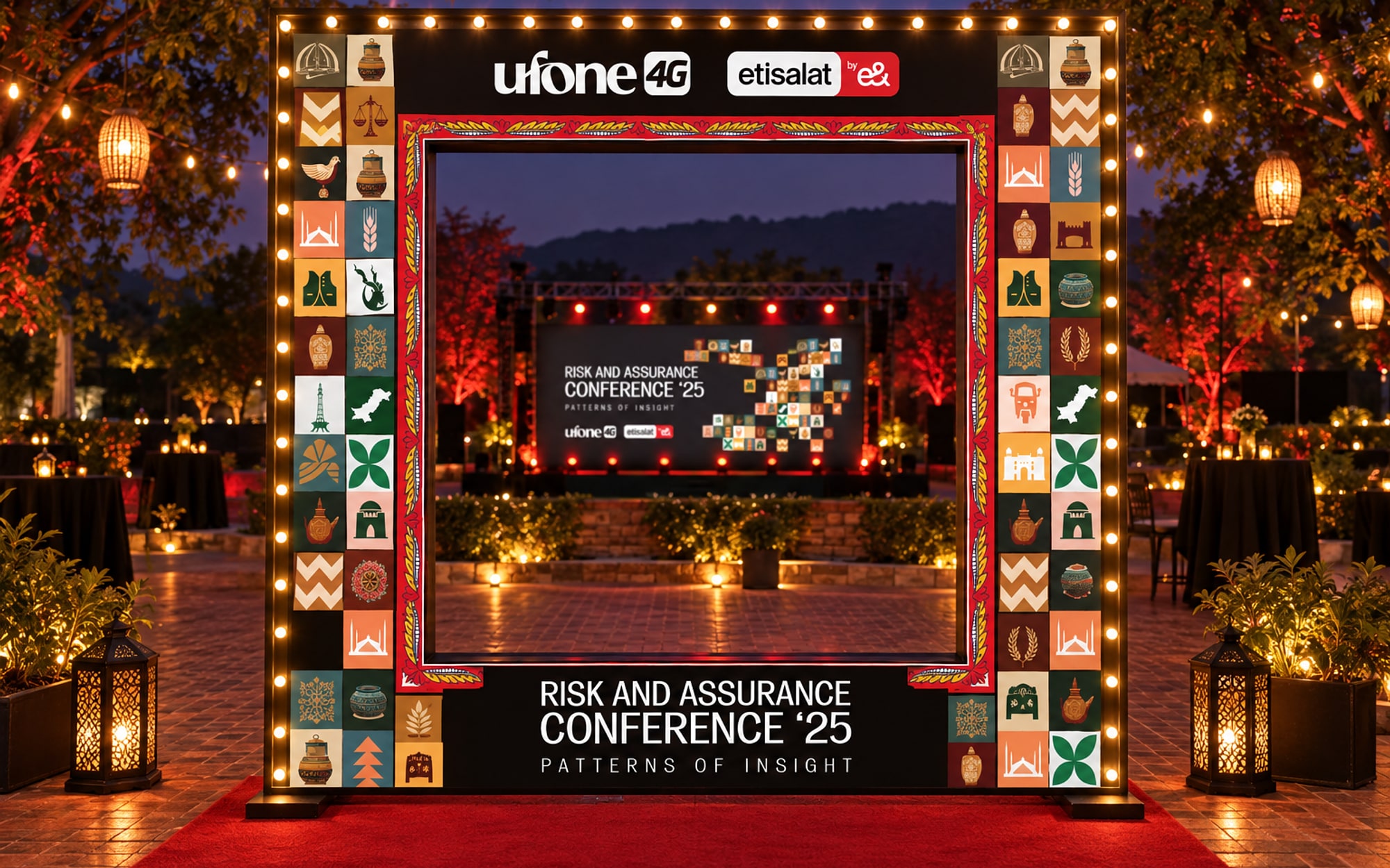A large black photo frame edged in bulbs and motif tiles on a red carpet, the lit stage visible through it