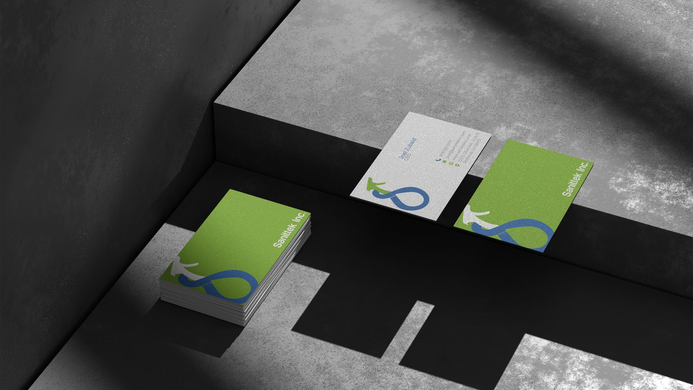A stack of Sanittek business cards and two loose cards arranged on grey concrete steps, lit from one side.
