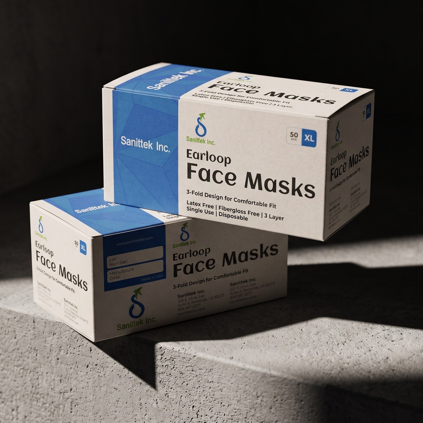 Two Sanittek face-mask cartons stacked on a concrete ledge in hard directional light.