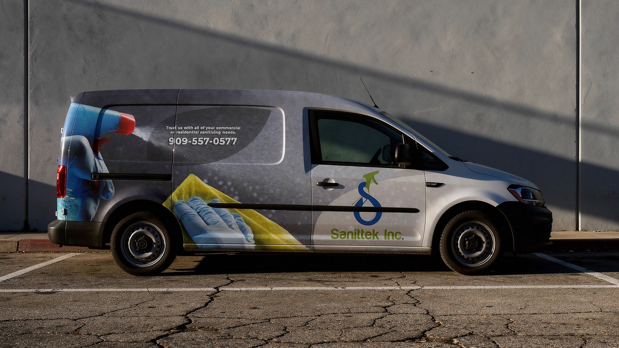 The Sanittek van in full side profile against a concrete wall, raking low sun, wrap and contact copy across the flank.