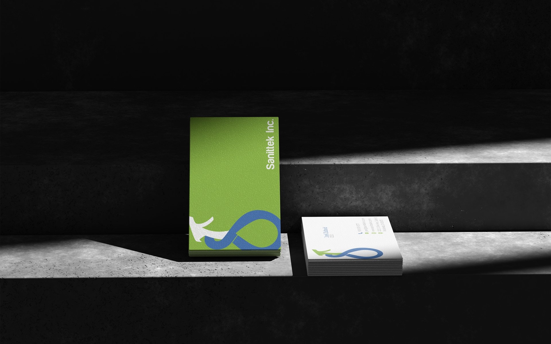 Sanittek business cards, green and white, standing on a concrete ledge in hard directional light.