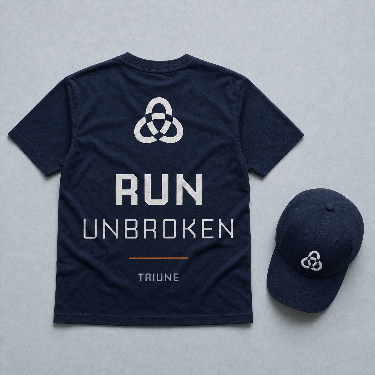 A navy t-shirt laid out back-side up with the mark small at the neck and RUN over UNBROKEN large below it, beside a matching navy cap with the mark embroidered on the front panel