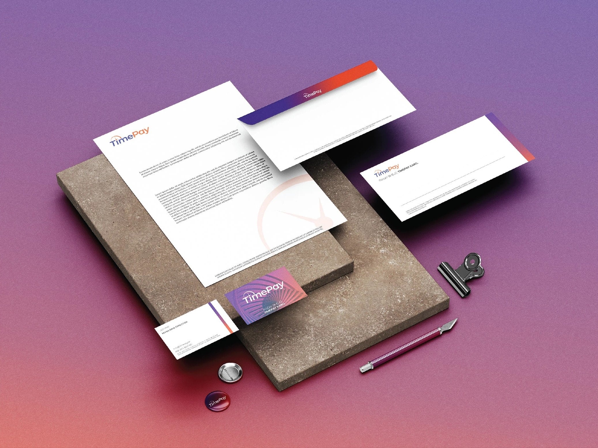 Letterhead, envelopes and business cards on stone slabs over a navy-to-red gradient, each carrying the logotype and a gradient band